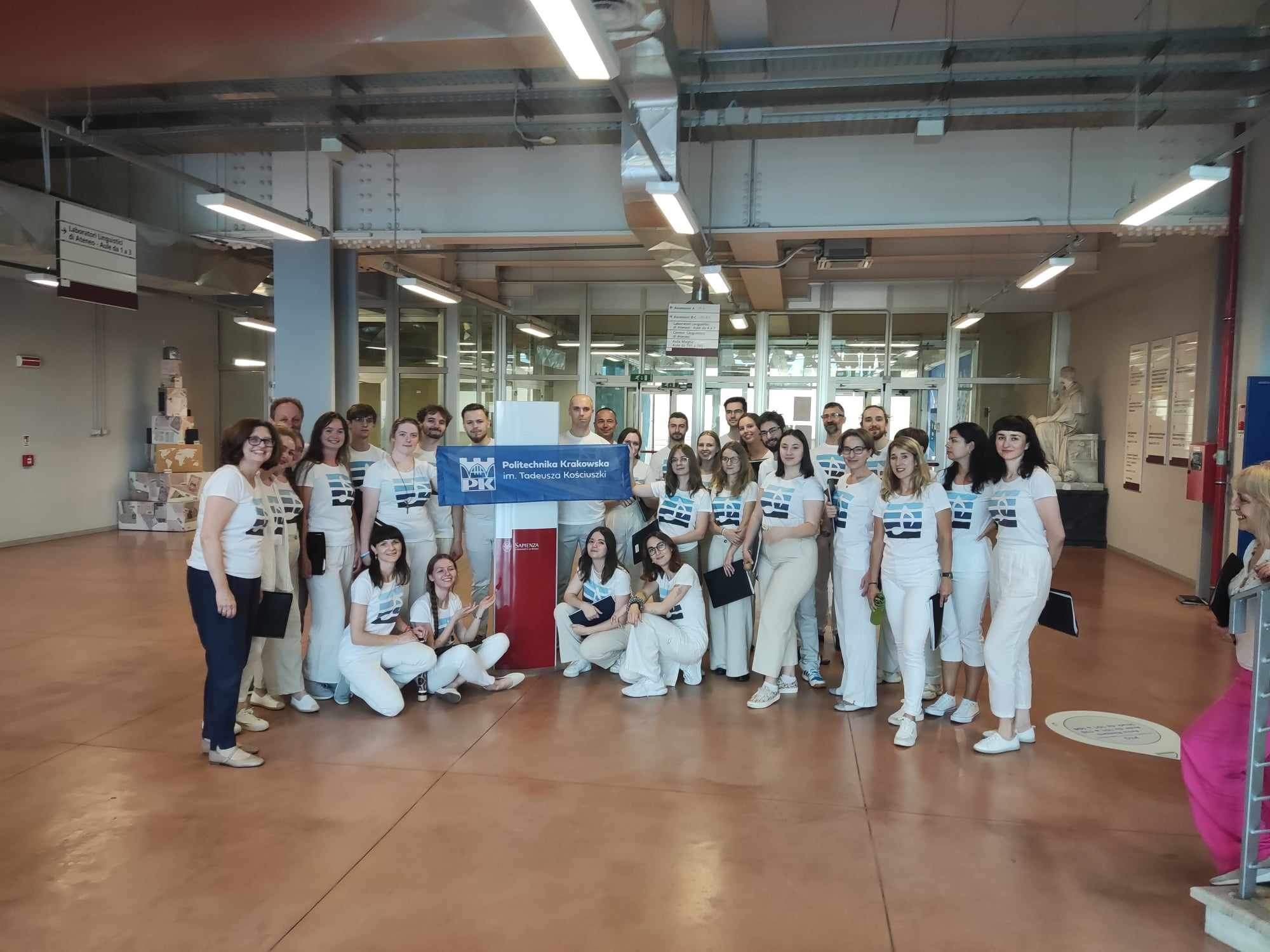 Występ Chóru na Uniwersytecie Sapienza w Rzymie. Chórzyści ubrani na biało -białe koszulki z logo Chóru i białe spodnie.