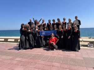 Zdjęcie grupowe Chóru "Cantata" w Hiszpanii, plener, deptak wzdłuż wybrzeża. W tle plaża i morze.