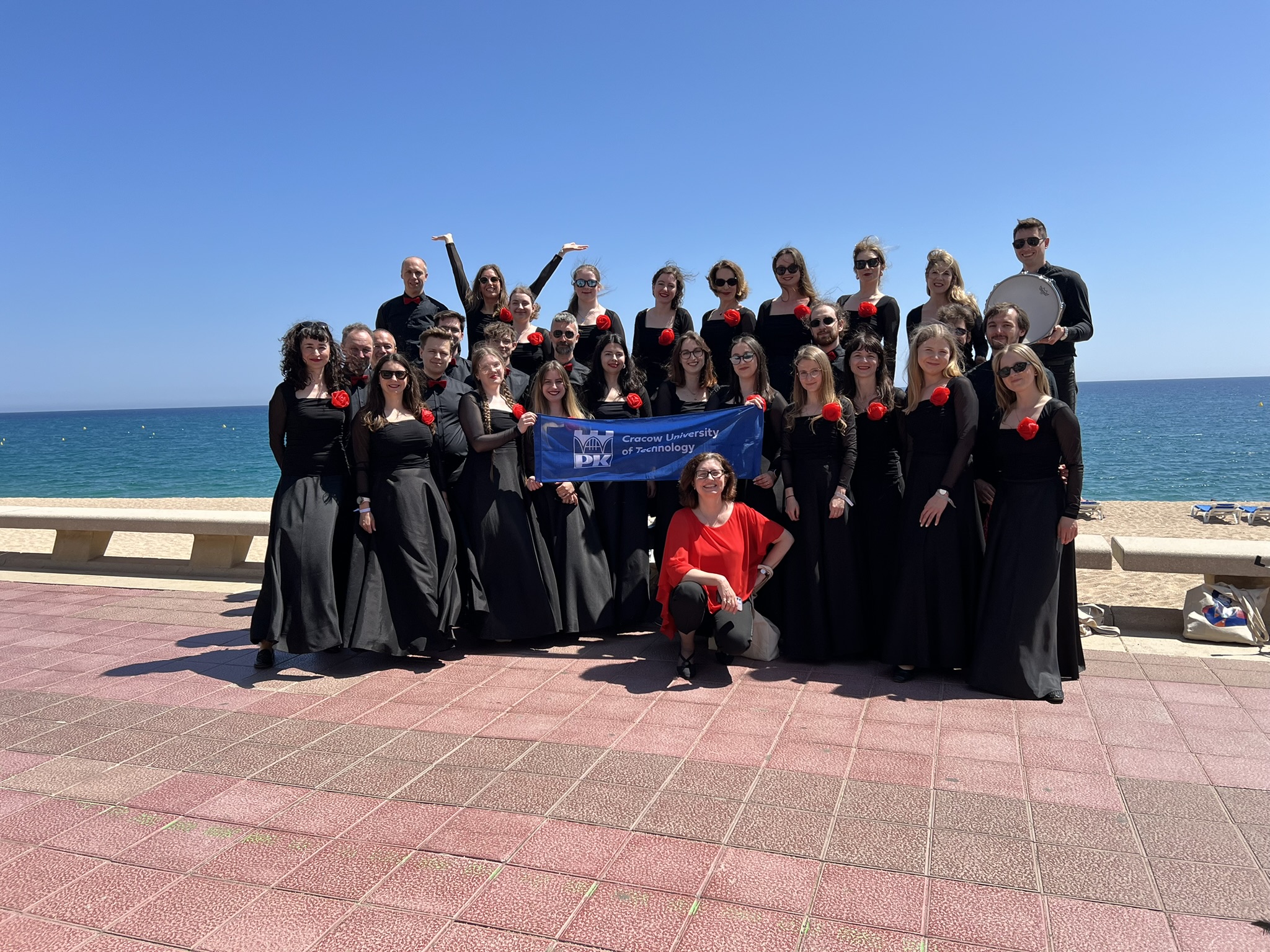 Zdjęcie grupowe Chóru "Cantata" w Hiszpanii, plener, deptak wzdłuż wybrzeża. W tle plaża i morze.