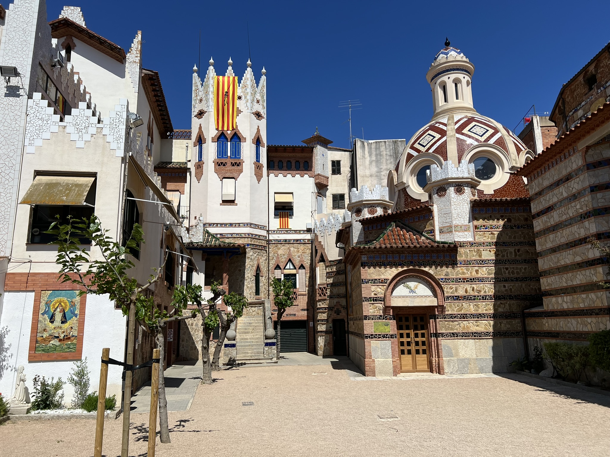 Zdjęcie przedstawiające dziedziniec, wejście do kaplicy chrzcielnej kościoła Església St. Romà oraz budynek obok kościoła w lloret de Mar, Hiszpania.