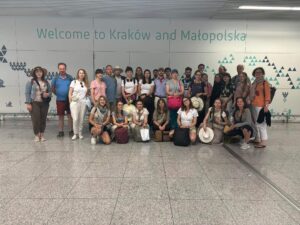 Zdjęcie Chóru na lotnisku w Balicach, po powrocie z Włoch, w tle napis na ścianie "Welcome to Kraków and Małopolska".