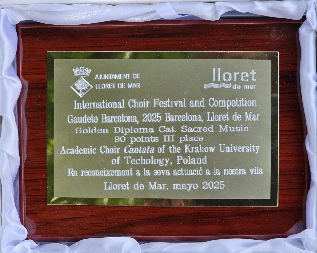 Zdjęcie nagrody zdobytej na festiwalu. Drewniana tabliczka z przyklejona złotą płytką, a na niej u góry po lewej stronie herb miasta z napisem: "AJUNTAMENT DE LLORET DE MAR", po prawej na górze logo miasta. Poniżej napisy: "International Choir Festival and Competition Gaudete Barcelona, 2025 Barcelona, Lloret de Mar Golden Diploma, Cat: Sacred Music 90 points III place Academic Choir Cantata of the Krakow University of Technology, Poland En reconeixement a la seva actuacio a la nostra vila Lloret de Mar, mayo 2025".